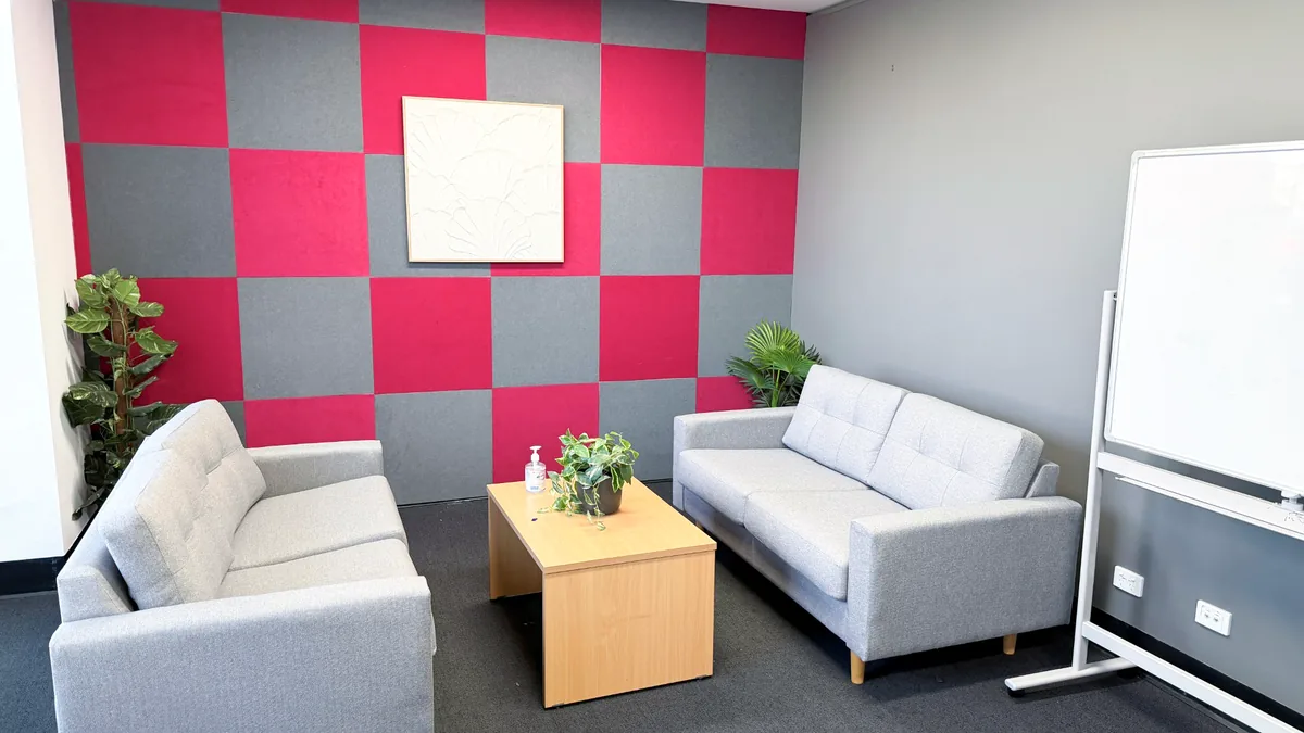 Counselling room with two lounges, a timber coffee table, plants and a pink and grey feature wall at ORS Fyshwick