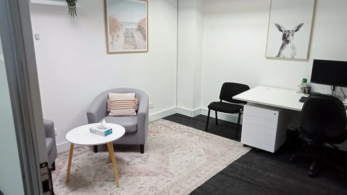 Consult and counselling room with a grey tub chair, coffee table, rug and clinician desk at ORS Jandakot