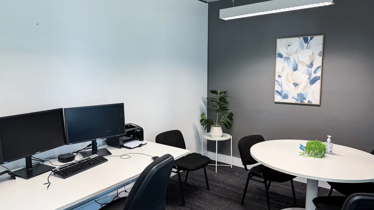 Consulting room with a round meeting table, clinician workstation and indoor plant at ORS Jandakot