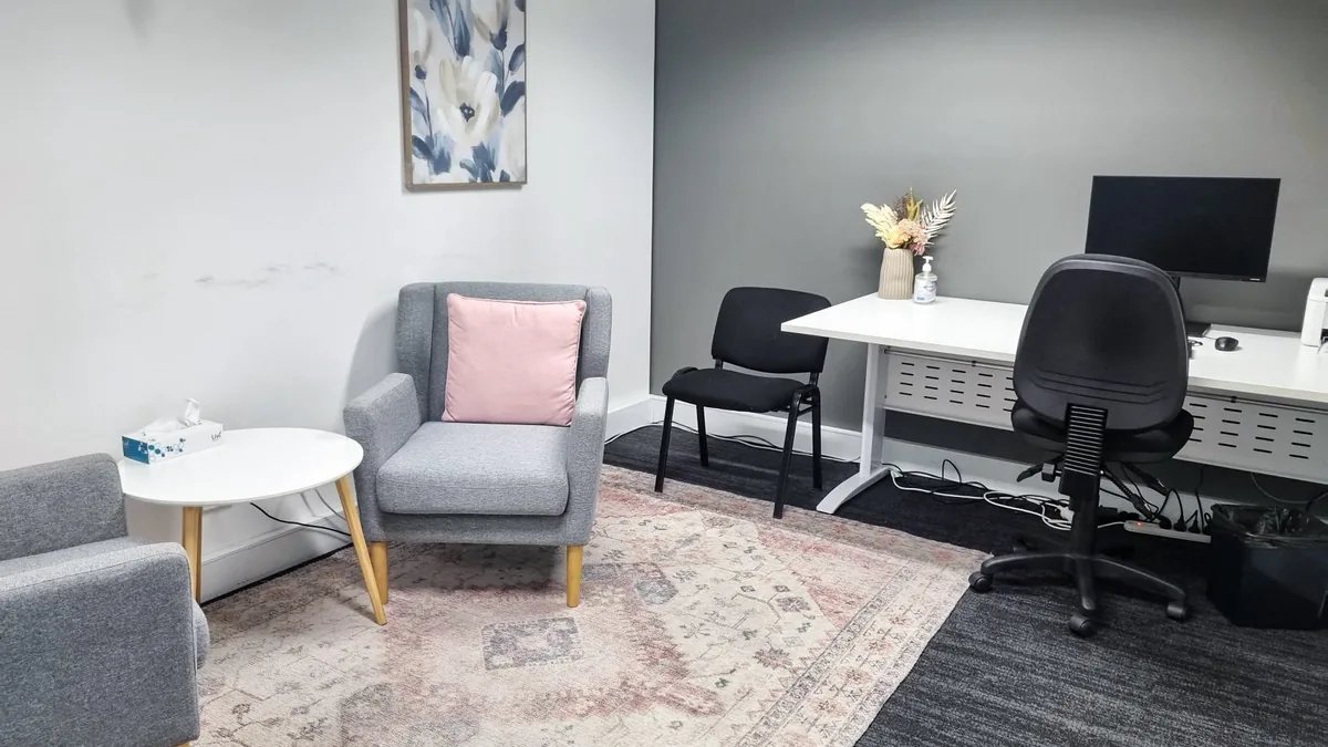 Counselling room with two armchairs, a patterned rug, coffee table and clinician desk at ORS Jandakot