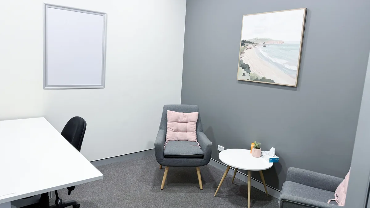 Counselling room with two armchairs, a pink cushion, side table and coastal artwork at ORS Mandurah