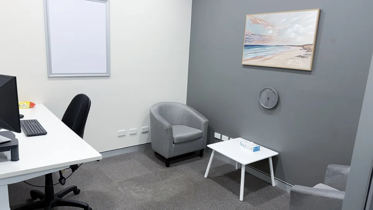 Counselling room with a tub chair, coffee table, clinician desk and beach artwork at ORS Mandurah