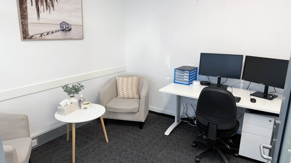 Counselling room with a tub chair, side table, clinician desk and coastal artwork at ORS Morley