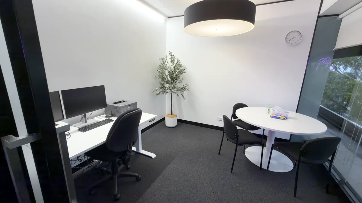 Appointment room with a round table, clinician workstation, pendant light and indoor tree at ORS Mount Waverley
