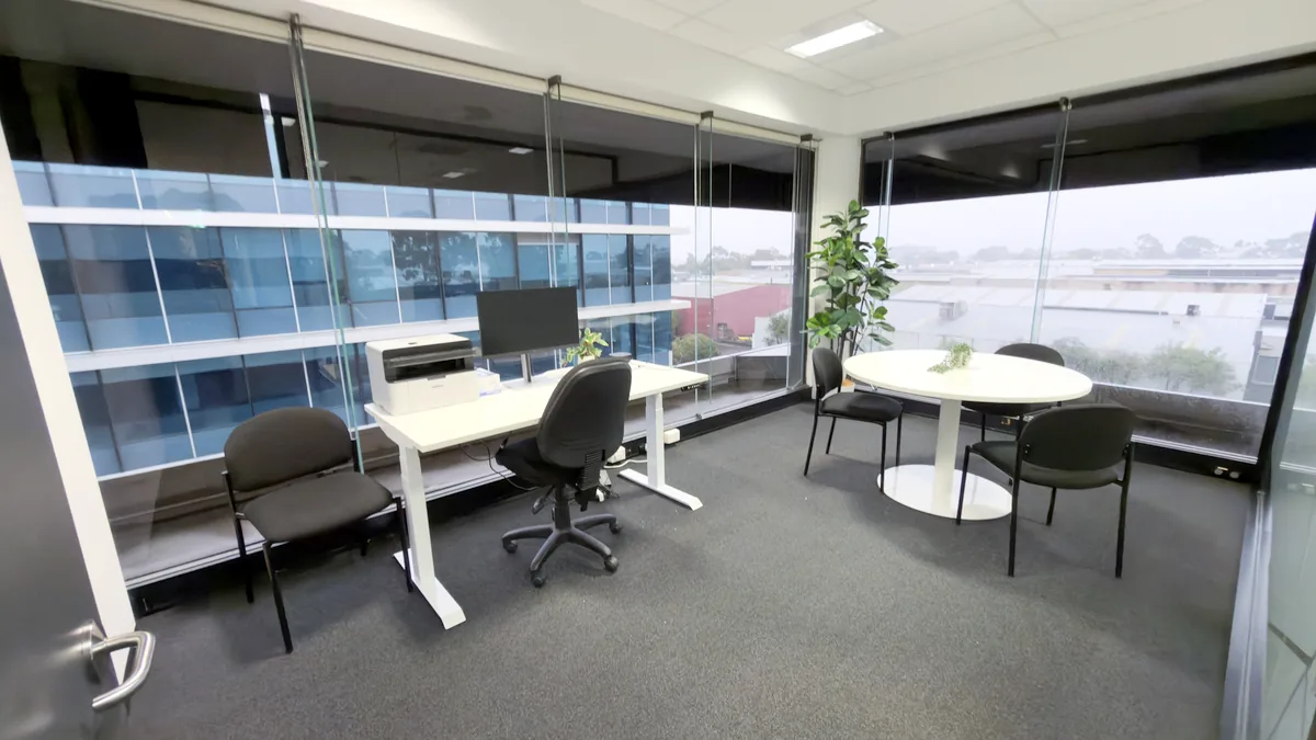 Consulting room with a clinician desk, round meeting table and wraparound windows at ORS Mount Waverley