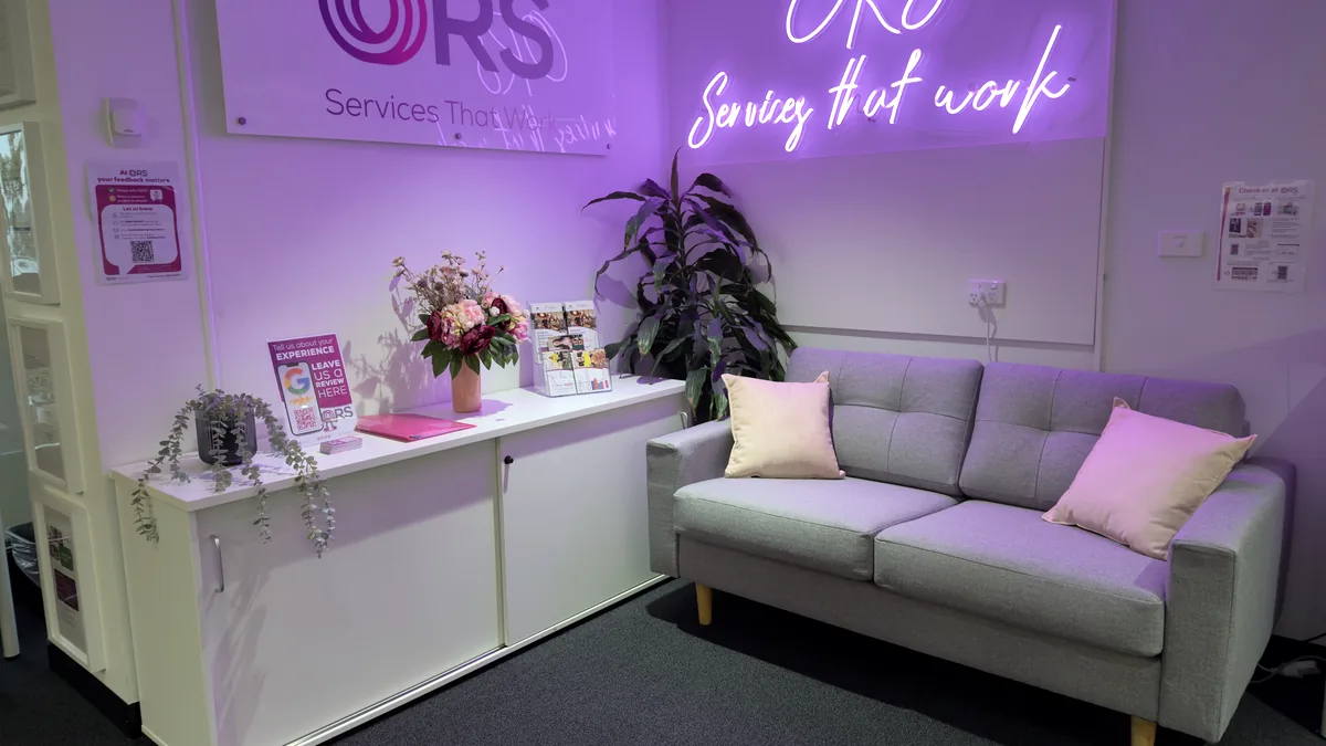 Waiting area with a grey lounge, pink cushions and a neon ORS Services that work sign at ORS Mount Waverley