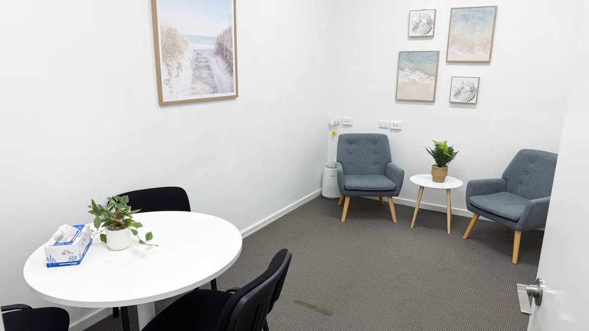 Appointment and counselling room with a round table, two armchairs and beach artwork at ORS Pakenham