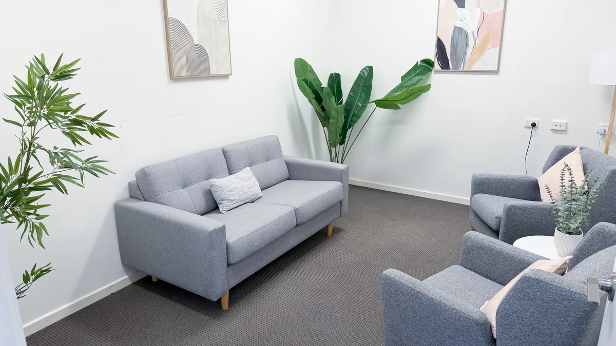 Counselling room with a grey lounge, two armchairs, cushions and indoor plants at ORS Pakenham