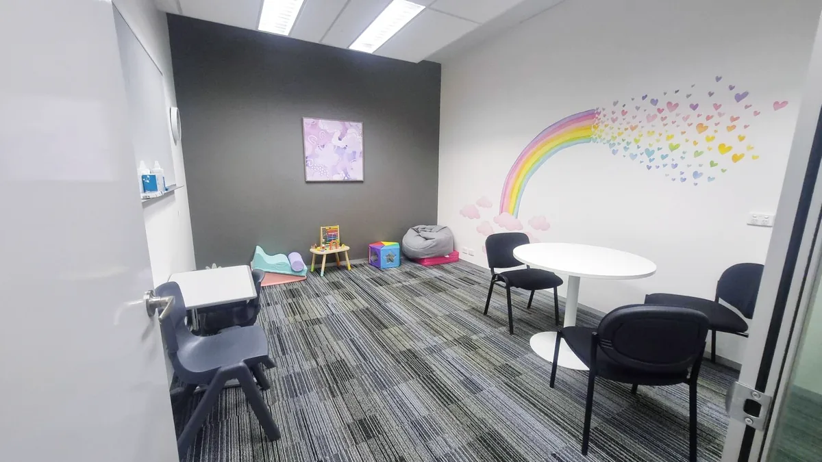 Paediatric therapy room with a rainbow wall mural, round table, child's desk and play equipment at ORS Stirling