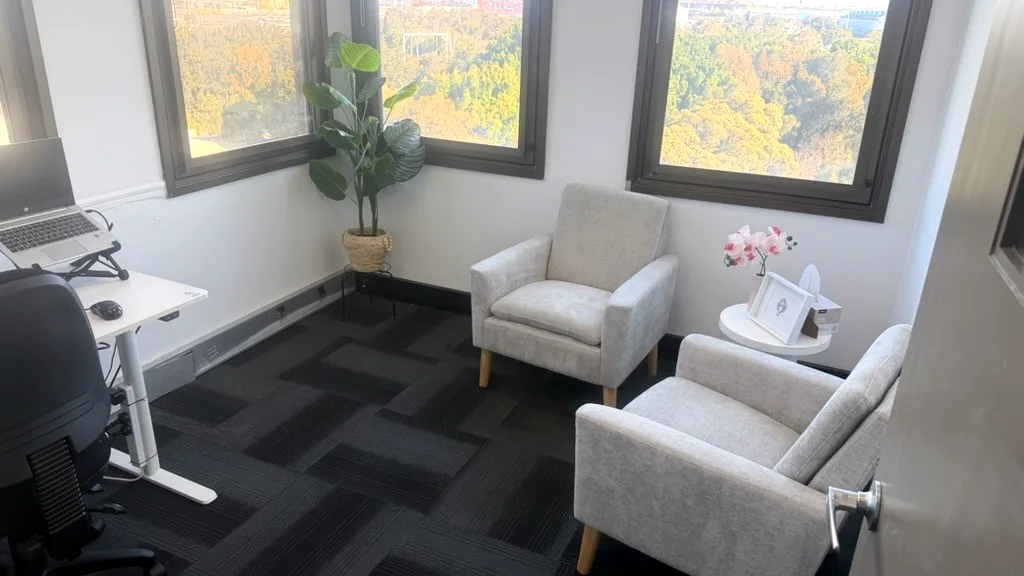 Counselling room with two armchairs, a side table and views over the treetops through tall windows at ORS Wollongong
