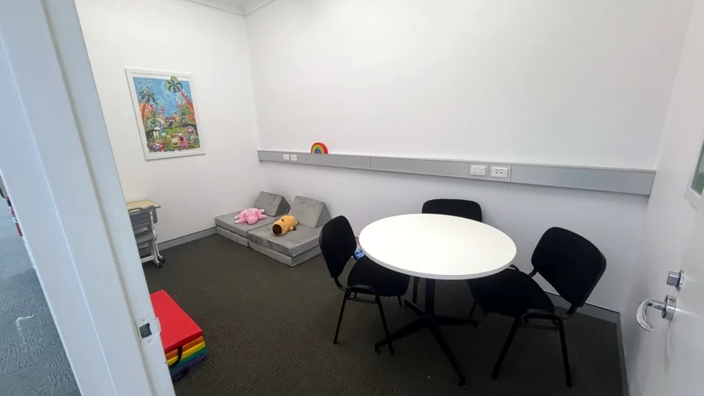 Paediatric therapy room with soft play cushions, a round table, chairs and a colourful artwork at ORS Wollongong