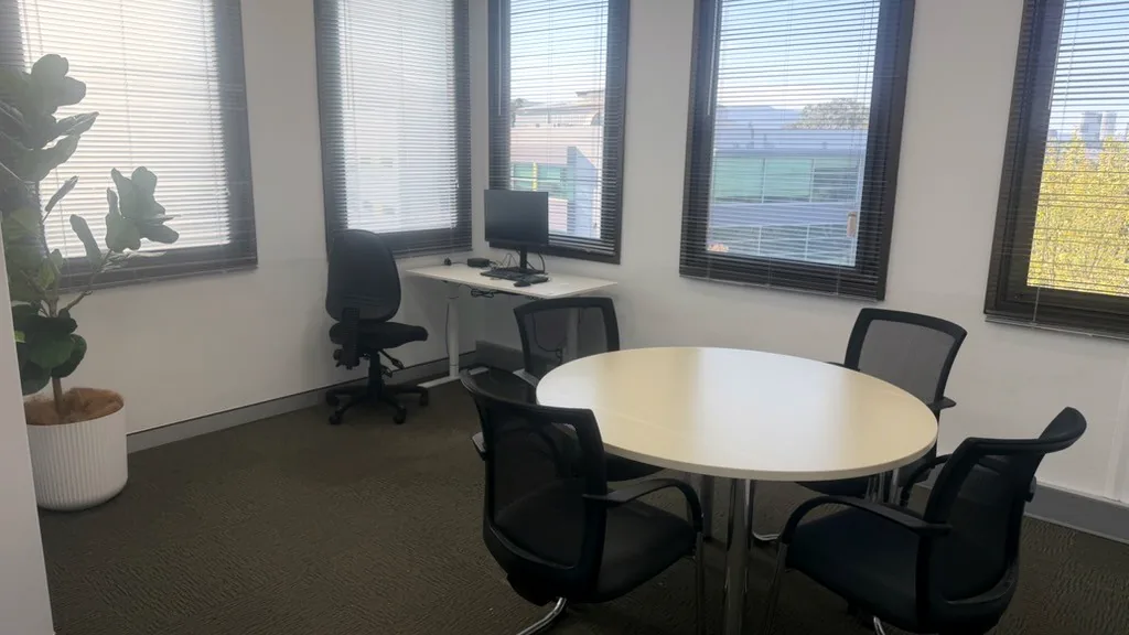 Telehealth and meeting room with a round table, mesh chairs, a clinician desk and tall windows at ORS Wollongong